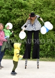 Animatorka na szczudłach rozdaje balony na patyczkach.