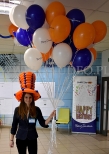 Hostessa w kapeluszu z balonów rozdaje balony reklamowe.