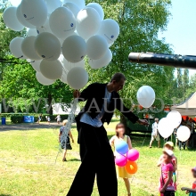 Szczudlarz rozdaje dzieciom balony z helem.