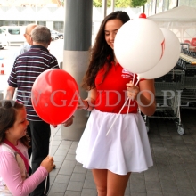 Hostessa rozdaje balony z nadrukiem założone na patyczki.