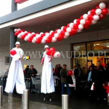 Girlanda nad wejściem do sklepu pod którą szczudlarze rozdają balony z nadrukiem.